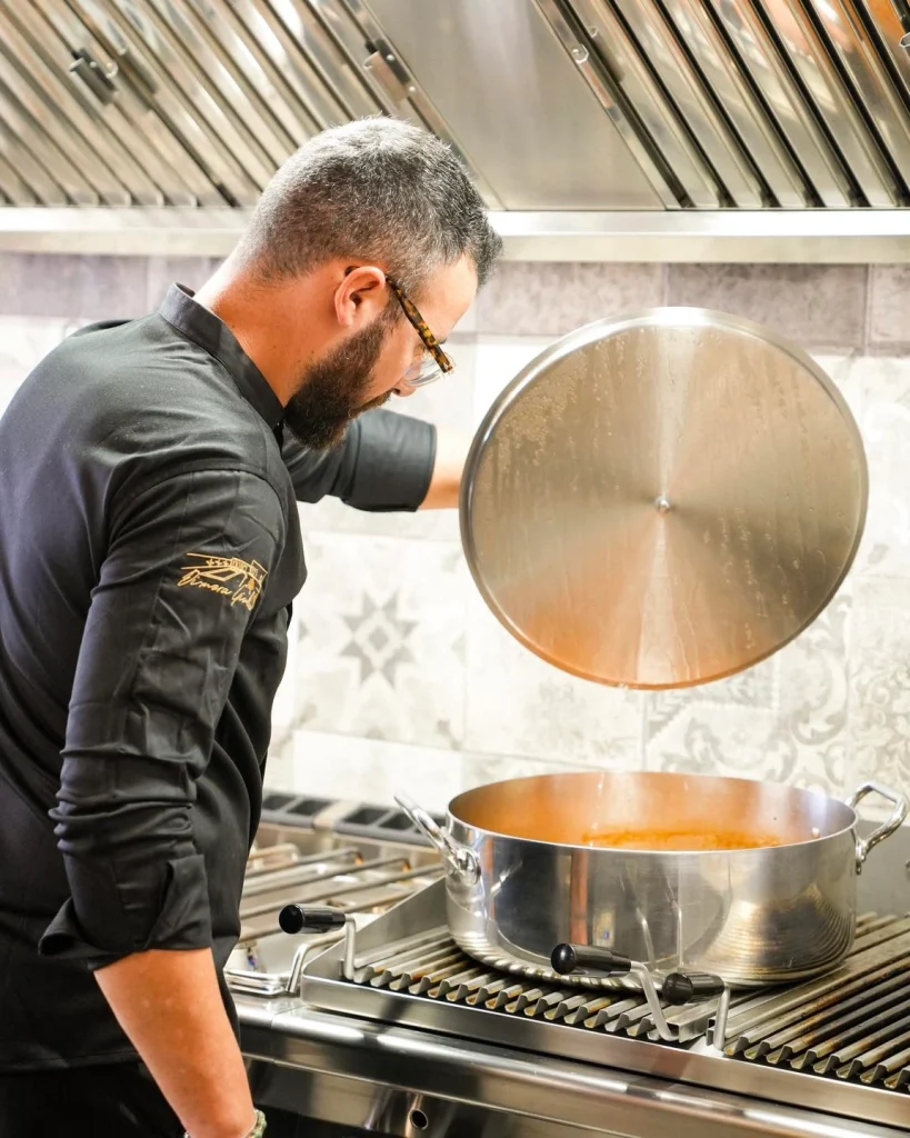 Chef solleva il coperchio di una pentola nella cucina professionale di Dimora Giulia